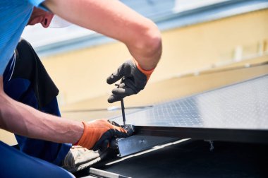 Evin çatısında fotovoltaik güneş paneli inşa eden bir işçi. Eldiven takan insan mühendislerine yakın çekim yapın. Güneş modülü takın. Dışarıdaki hex anahtarının yardımıyla. Yenilenebilir enerji üretimi kavramı.