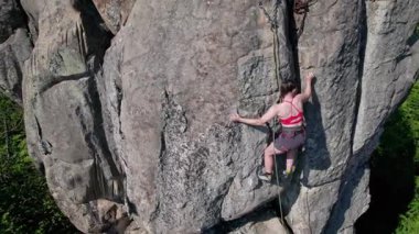 Kadın kaya tırmanışçısının, güvenlik için kayış takımı ve iple engebeli kireçtaşı kayalıklara tırmanışının hava görüntüsü. Sporcu kadın Ukrayna 'nın Karpatya dağlarındaki Dobvush Kayaları' nda dikey büyük kayalara tırmanıyor..