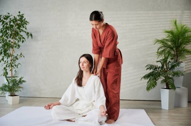 Masör Tayland yogası masajı yapıyor. Kadın terapist, kadın hasta için evde geleneksel masaj tedavisi uyguluyor. Müşteri mindere oturuyor, meditasyon yapıyor, sakin bir atmosferde el masajının keyfini çıkarıyor..