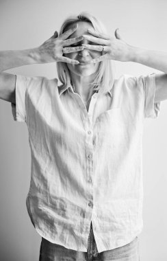 Güzel bir kadın elinde yüzünü saklıyor. Güzel dişinin parmakları yüzünü kaplıyor. Hafif arka planda poz veren gündelik kıyafetli genç bir kadın. Siyah ve beyaz resim.