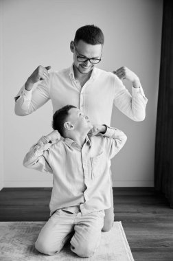 Genç baba meraklı oğluyla oynuyor. Komik çocuk babasına kaslarını gösteriyor. Aile evde aktivite oyunlarını seviyor. Siyah ve beyaz resim.