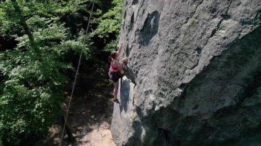 Kadın kaya tırmanışçısının, güvenlik için kayış takımı ve iple engebeli kireçtaşı kayalıklara tırmanışının hava görüntüsü. Sporcu kadın Ukrayna 'nın Karpatya dağlarındaki Dobvush Kayaları' nda dikey büyük kayalara tırmanıyor..