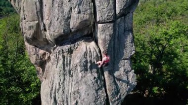 Kadın kaya tırmanışçısının, güvenlik için kayış takımı ve iple engebeli kireçtaşı kayalıklara tırmanışının hava görüntüsü. Sporcu kadın Ukrayna 'nın Karpatya dağlarındaki Dobvush Kayaları' nda dikey büyük kayalara tırmanıyor..