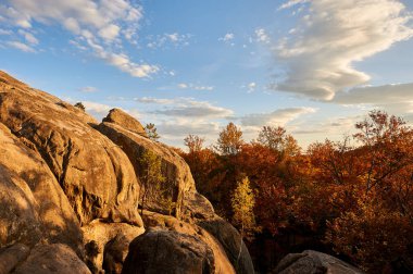 Batan güneşin altın renkleri kayalık oluşumları ve sonbahar yapraklarını aydınlatarak olay yerine sıcak bir parıltı saçar. Aşağıda canlı portakallar ve kırmızı ağaçlar var. Dovbush Kayaları, Karpat Dağları, Ukrayna, Avrupa.