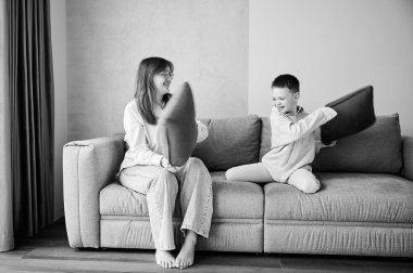 İki küçük kardeş kanepede yastık savaşı başlattı. Küçük oğlan ve ablası evde yastıklarla kavga ediyorlar. Aileyle eğlenceli vakit geçirmek. Siyah ve beyaz resim.