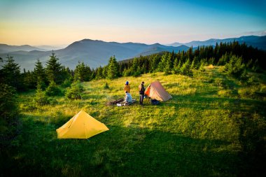 Sabahları iki çadırı olan manzaralı dağ kampı. İki kampçı, bulutsuz gökyüzünün altında yuvarlanan dağların huzurlu manzarasının keyfini çıkarıyorlar. Resimli gündoğumu manzarası, huzurlu ve rahat bir açık hava deneyimi yaratıyor..