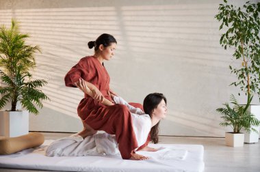 Masör Tayland yogası masajı yapıyor. Geleneksel masaj tedavisi uygulayan kadın terapist, kadın hastaların vücudunu geriyor. Müşteri paspasın üzerinde uzanıyor, sakin atmosferde el masajının keyfini çıkarıyor..