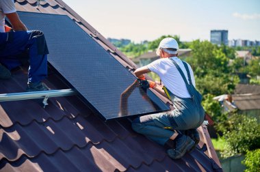İşçiler evin çatısına güneş paneli inşa ediyorlar. Dışarıda fotovoltaik güneş modülü kuran kask takan iki adam. Alternatif, yeşil ve yenilenebilir enerji üretimi kavramı.
