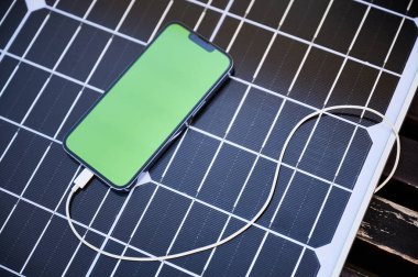 Yeşil ekranlı akıllı telefon şarj kablosu ile güneş paneline bağlandı. Görüntü, yenilenebilir ve taşınabilir enerji çözümlerini vurgulayarak, elektronik cihazları şarj etmek için güneş enerjisinin kullanımını vurguluyor.