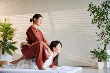 Masör Tayland yogası masajı yapıyor. Geleneksel masaj tedavisi uygulayan kadın terapist, kadın hastaların vücudunu geriyor. Müşteri paspasın üzerinde uzanıyor, sakin atmosferde el masajının keyfini çıkarıyor..