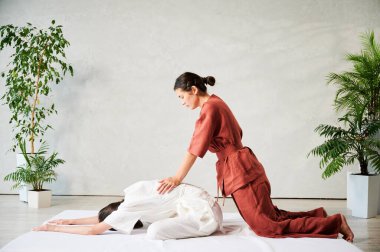 Masör Tayland yogası masajı yapıyor. Geleneksel masaj tedavisi uygulayan kadın terapist, kadın hastaların vücudunu geriyor. Müşteri paspasın üzerinde uzanıyor, sakin atmosferde el masajının keyfini çıkarıyor..