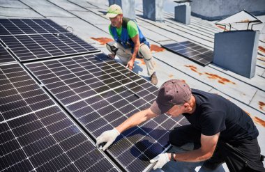 İşçiler evin metal çatısında güneş paneli inşa ediyorlar. İki adam dışarı fotovoltaik güneş modülü kuruyor. Alternatif, yeşil ve yenilenebilir enerji üretimi kavramı.