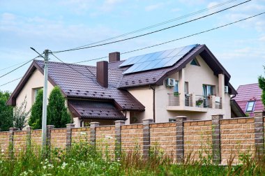 Çatıda fotovoltaik etkiyle elektrik üretmek için güneş panelleri olan bir ev. Çatıda güneş enerjisi sistemi olan bir ev. Alternatif enerji kavramı, özerklik, güç sürdürülebilir kaynaklar.