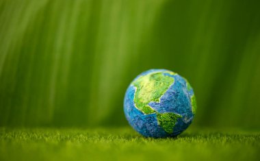 World Earth Day Concept. Green Energy, ESG, Renewable and Sustainable Resources. Environmental Care. Globe against on Green Grass and Leaf. Side View