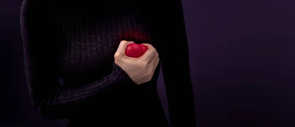 Painful, Heart Attack Concept. Young Woman Squeezed a Red Plastic Heart against her Chest. Heart Disease or feeling very Heartbreak and Sorrow