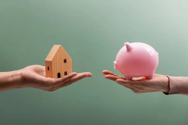 Financial Goals Concept, Buying a New House with Savings Money. two person Holding a Piggy Bank and a Wooden House for Swap eachother