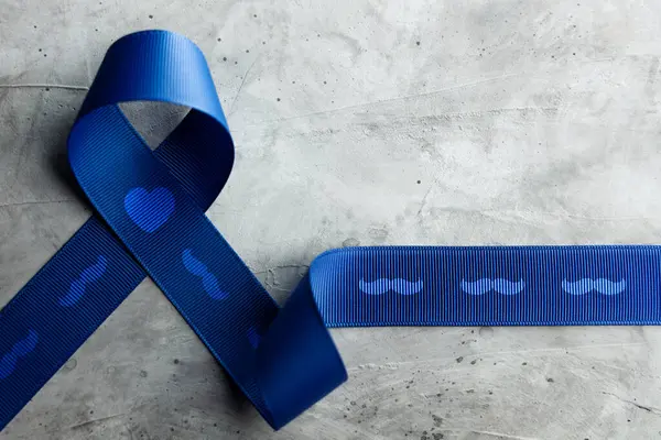 Prostate Cancer Awareness Campaign Concept. Men Healthcare. Close up of a Blue Moustache Ribbon  Lying on Rough Grey Cement Concrete background, Top View