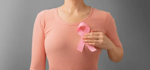 Breast Cancer Awareness Campaign Concept. Women Healthcare. Close up of a Young Female Touching Pink Ribbon on her Thorax