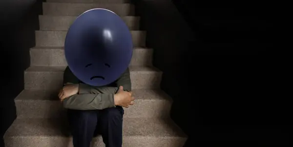 精神健康概念 一个紧张 抑郁的人和一个气球坐在楼梯上 负面的情绪和感觉 黑暗的声音 图库图片