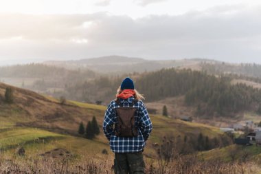 Sırtında bir sırt çantasıyla turist yürüyüşçüsü güzel bir dağ manzarasının arka planında duruyor ve uzaklığa bakıyor. Ekstrem sporlar, turizm. Yaz tatili.