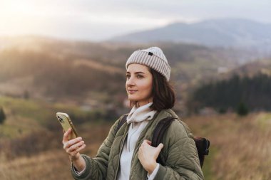 Mutlu gülümseyen kadın fotoğrafçı doğanın akıllı telefonuyla fotoğraf çekiyor ve dağdaki ormanda seyahat ederken kamerasında kuşlar var.