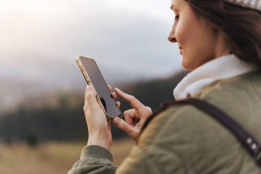 Ormanda yürürken cep telefonunda internet haritası kullanan kadın yolcuların modern cep telefonu cihazını tutan ve parmağıyla işaret eden kadın ellerinin ekili fotoğrafı.