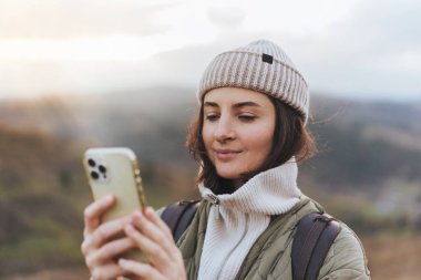 Çevrimiçi harita ile cep telefonu kullanan mutlu gülümseyen kadın gezginin portresi ve arkadaşlarına mesaj atmak, arka planda bulanık orman ve dağlar, doğada teknoloji kullanma kavramı