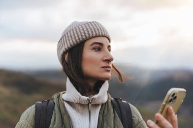 Gün batımında bir dağın tepesinde cep telefonu kullanan güzel bir kadın..