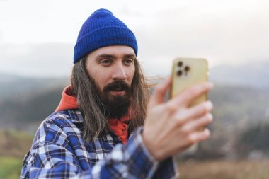 Genç yürüyüşçü dağın tepesinde selfie portresi çekiyor. Mutlu adam kameraya gülümsüyor. Yürüyüş, spor, seyahat ve teknoloji konsepti.