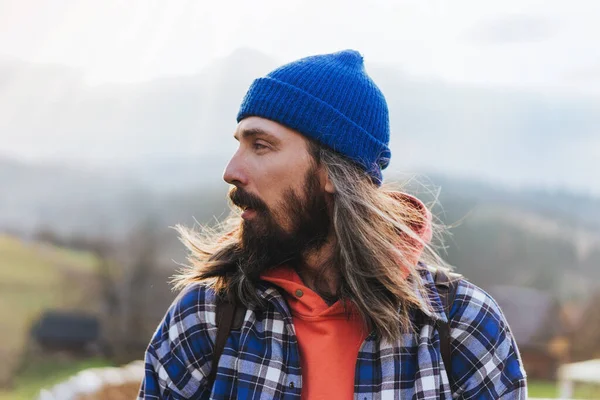 青い帽子 スウェットシャツを身に着けている長い髪を持つヒップスター男性の肖像画とハイキング中に背景に山とジャケットを果たした — ストック写真