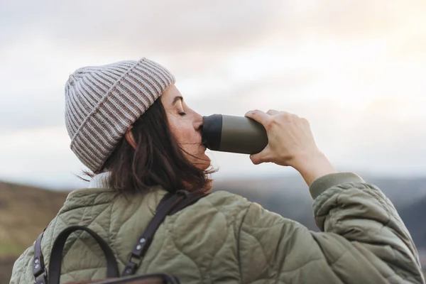 stock image Woman standing on the cliff and drinking water. Female mountaineer looking at beautiful view with a water bottle in hand.