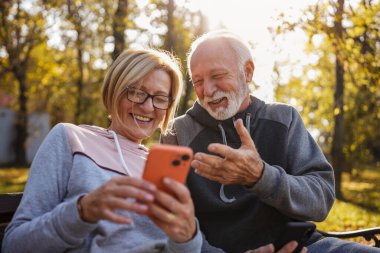 senior couple spending time together in park with phones