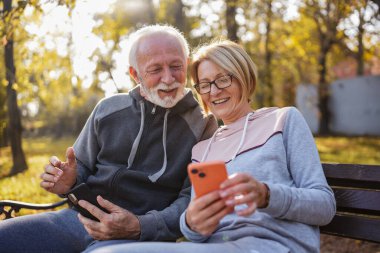 senior couple spending time together in park with phones