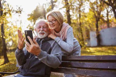 senior couple spending time together in park with phones