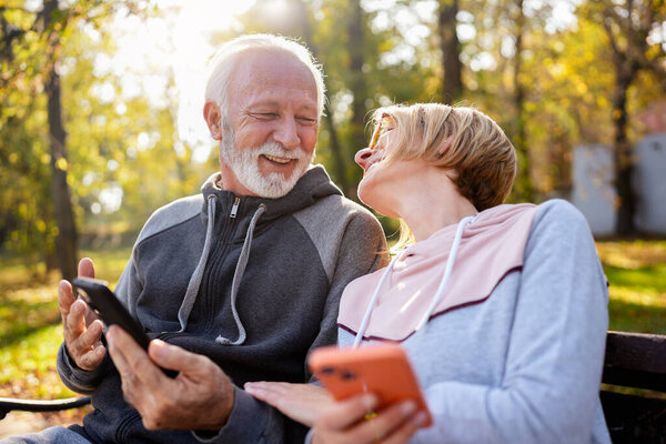 senior couple spending time together in park with phones