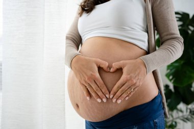 Hamile kadın pencerenin yanında duruyor, poz veriyor.