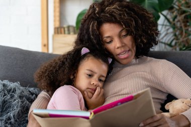 Afrikalı Amerikalı kız ve anne kitap okuyor.