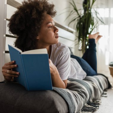 Afro-Amerikan kadın evde kitap okuyor.