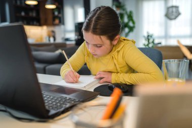 Kulaklık takan sevimli çocuk internetten öğrenmek için laptop kullanıyor. Ev okulu. Evde ödev yapan bir kız. Evde eğitim için yaşam tarzı konsepti. Sosyal uzaklık ve eğitim.