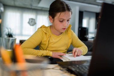 Kulaklık takan sevimli çocuk internetten öğrenmek için laptop kullanıyor. Ev okulu. Evde ödev yapan bir kız. Evde eğitim için yaşam tarzı konsepti. Sosyal uzaklık ve eğitim.