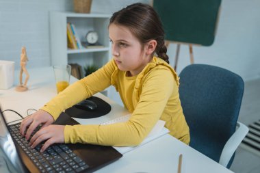 Kulaklık takan sevimli çocuk internetten öğrenmek için laptop kullanıyor. Ev okulu. Evde ödev yapan bir kız. Evde eğitim için yaşam tarzı konsepti. Sosyal uzaklık ve eğitim.