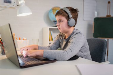 Kulaklık takan sevimli çocuk internetten öğrenmek için laptop kullanıyor. Ev okulu. Çocuk evde ödev yapıyor. Evde eğitim için yaşam tarzı kavramı