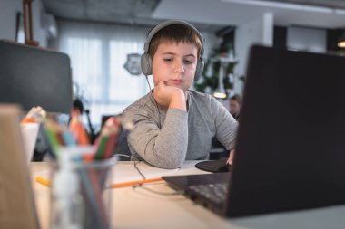 Kulaklık takan sevimli çocuk internetten öğrenmek için laptop kullanıyor. Ev okulu. Çocuk evde ödev yapıyor. Evde eğitim için yaşam tarzı kavramı
