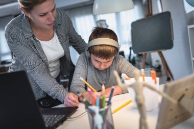 Anne, çocuğun dizüstü bilgisayarın önünde ödevlerini yapmasına yardım ediyor. Yaşam tarzı konsepti evde eğitim.