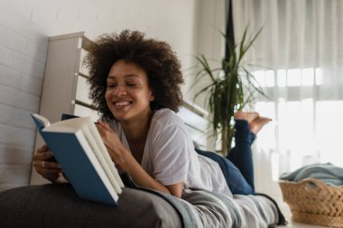Afro-Amerikan kadın evde kitap okuyor.