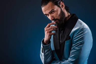 Güzel, erkeksi, sakallı genç bir adam elinde bir şişe parfüm tutuyor. Erkek parfümü, takım elbiseli sakallı bir adam..