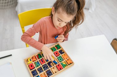 Küçük liseli kız tahta harflerle oynuyor. Yazmayı öğrenmek.