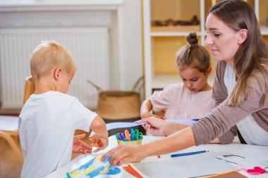Öğretmen bazı kağıt işlerinde çocuklara yardım eder. Yürümeye başlayan çocuklar ve anaokulu öğrencileri için iyi motor becerileri geliştirmek