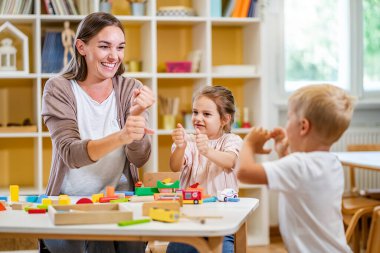 Kindergarten teacher playing together with children at colorful preschool classroom. Mother playing with children. clipart