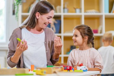 Renkli anaokulu sınıfında anaokulu öğretmeni çocukla birlikte oynuyor. Anne çocukla oynuyor.
